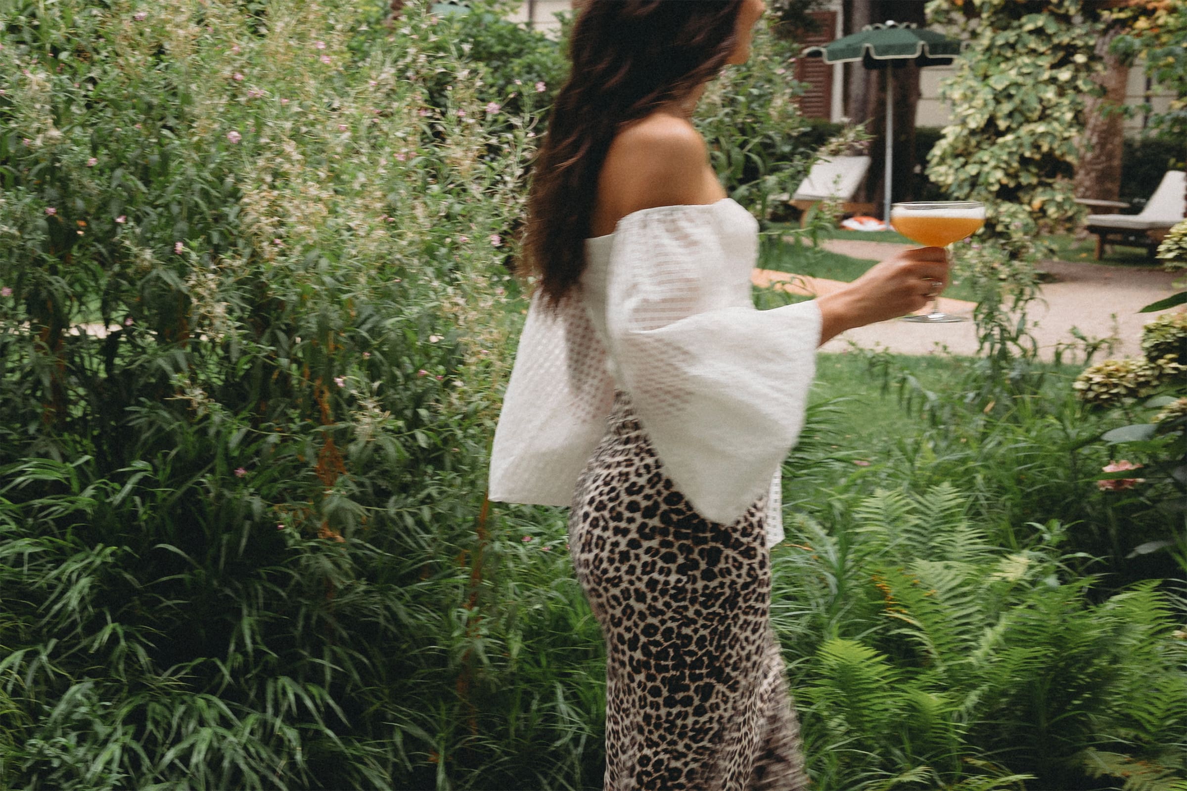 Una donna passeggia per un giardino con in mano il cocktail Amarill Sour.