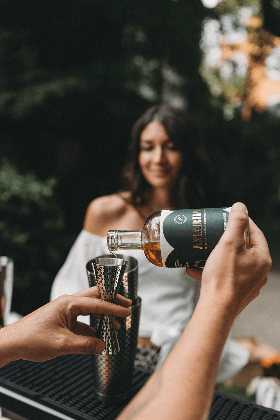 Ein Barkeeper mixt einen Cocktail an der Theke und gießt Amaro Amarill in einen silbernen Messbecher.