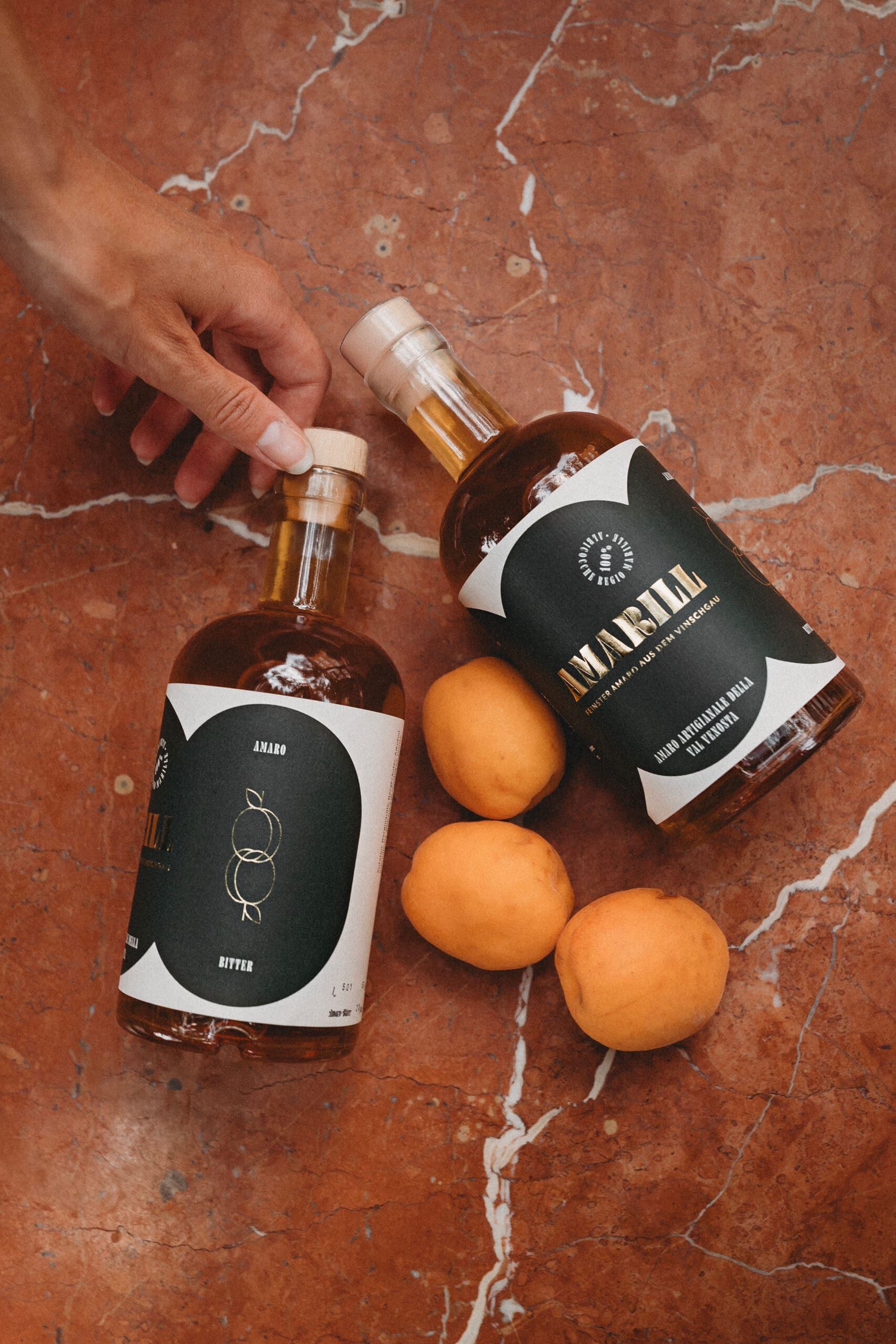Zwei Flaschen Amaro Amarill und drei Marilllen kunstvoll drapiert auf einem Marmortisch.