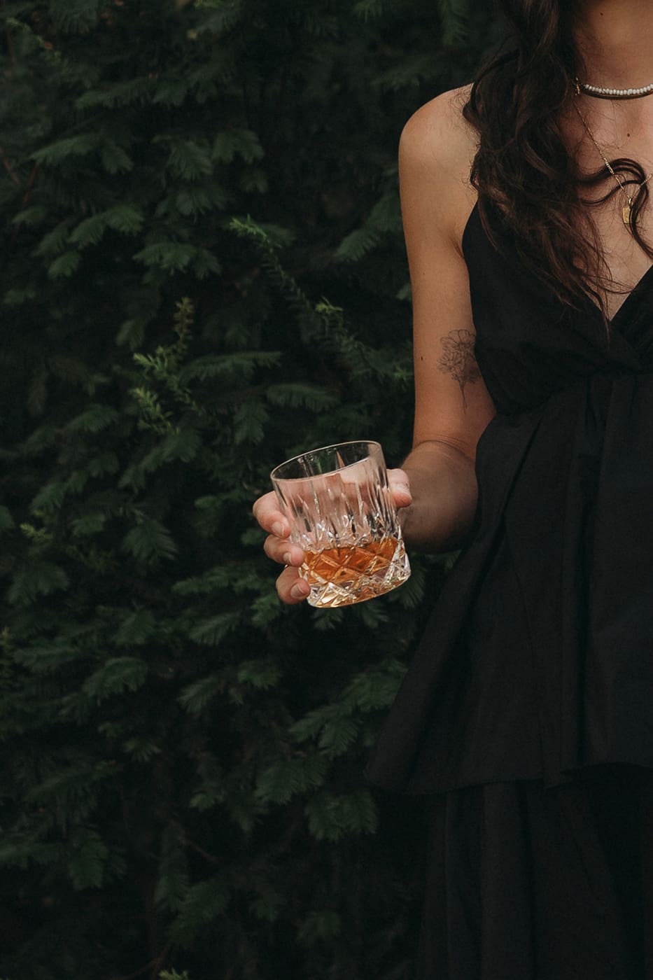 Una donna in abito nero tiene in mano un bicchiere tumbler basso con Amaro Amarill puro con ghiaccio.