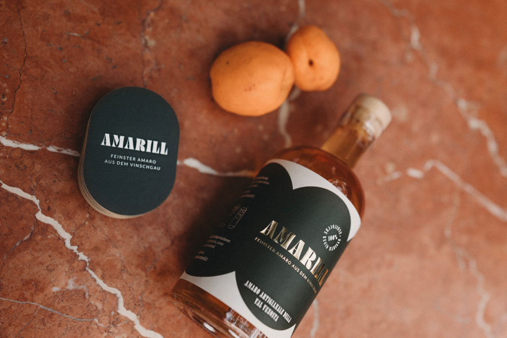 Eine Flasche Amaro Amarill, zwei Marillen und ein Stapel Visitenkarten von Amaro Amarill kunstvoll drapiert auf einem Marmortisch.