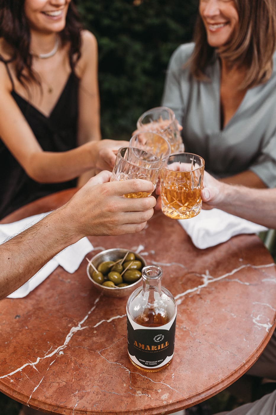 Vier Menschen stoßen mit Amaro Amarill pur auf Eis an, auf dem Tisch steht eine Flasche Amaro Amarill.