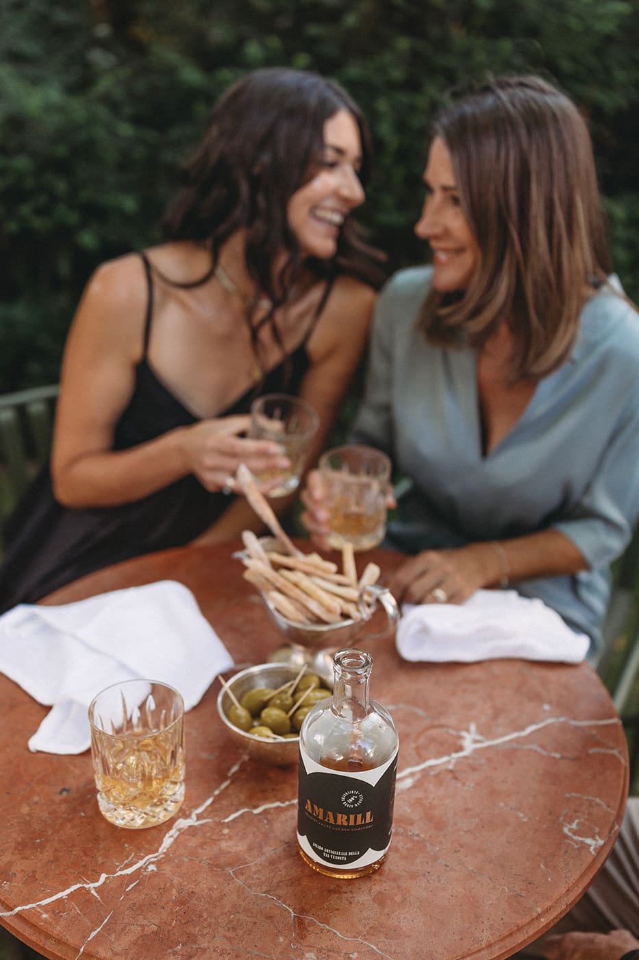 Zwei Frauen sitzen lachend am Tisch und trinken Amaro Amarill zum Digestif pur auf Eis.