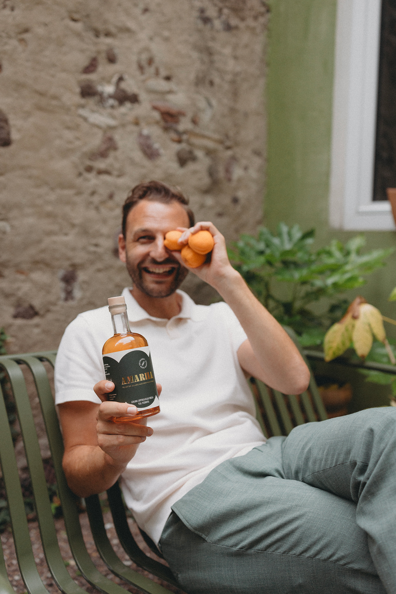 David Frank, Gründer von Amario Amarill, präsentiert eine Flasche Amaro Amarill und hält sich lachend drei Vinschger Bergmarillen vor das Gesicht.